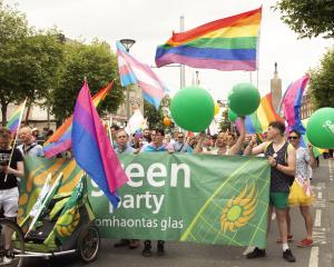 A large group waving rainbow flags gathers behind a Green Party banner to take part in a Pride parade