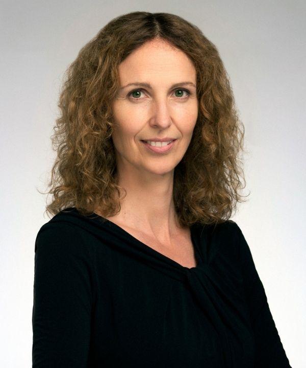 A woman with brown curly hair, Vanessa Liston, wearing a black v-neck top.