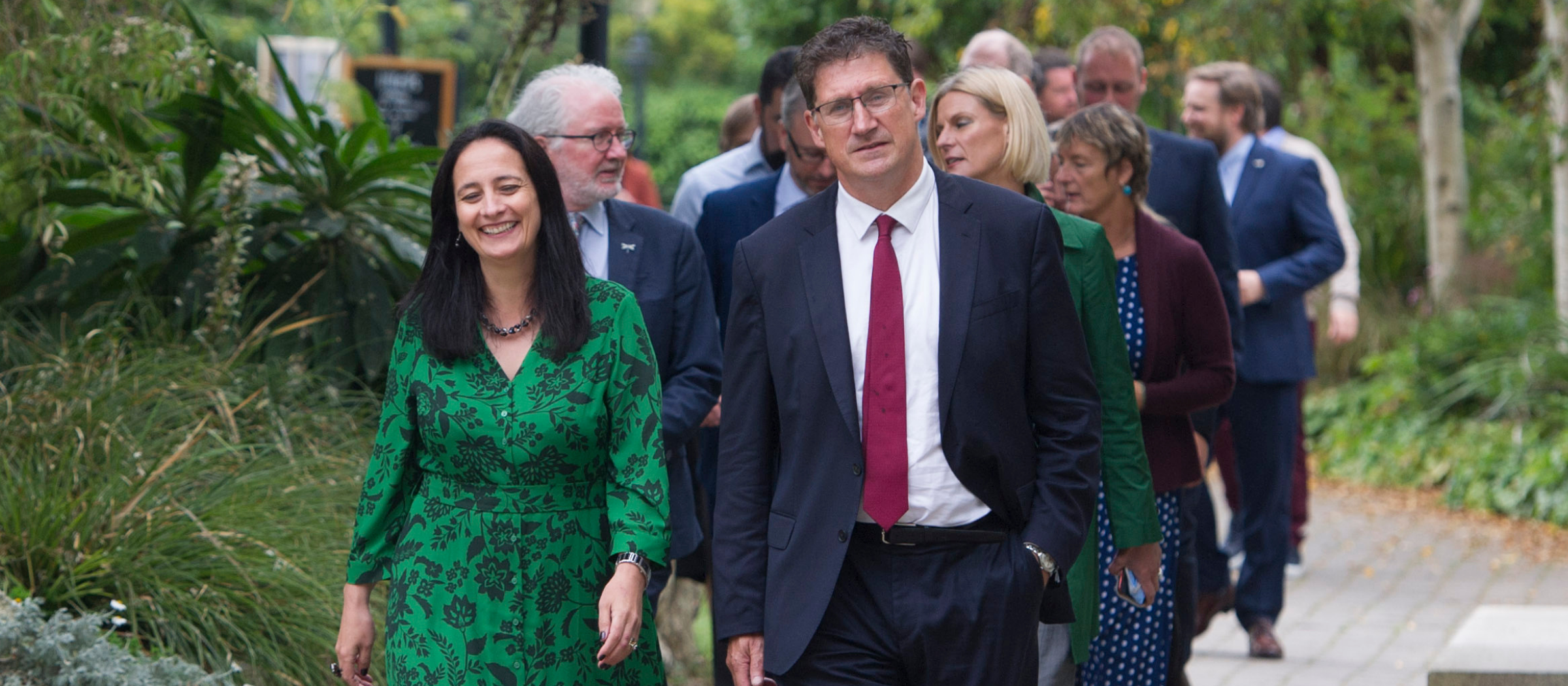 A photo of a group of people walking in twos along a path in a park. At the front is Catherine Martin and Eamon Ryan.