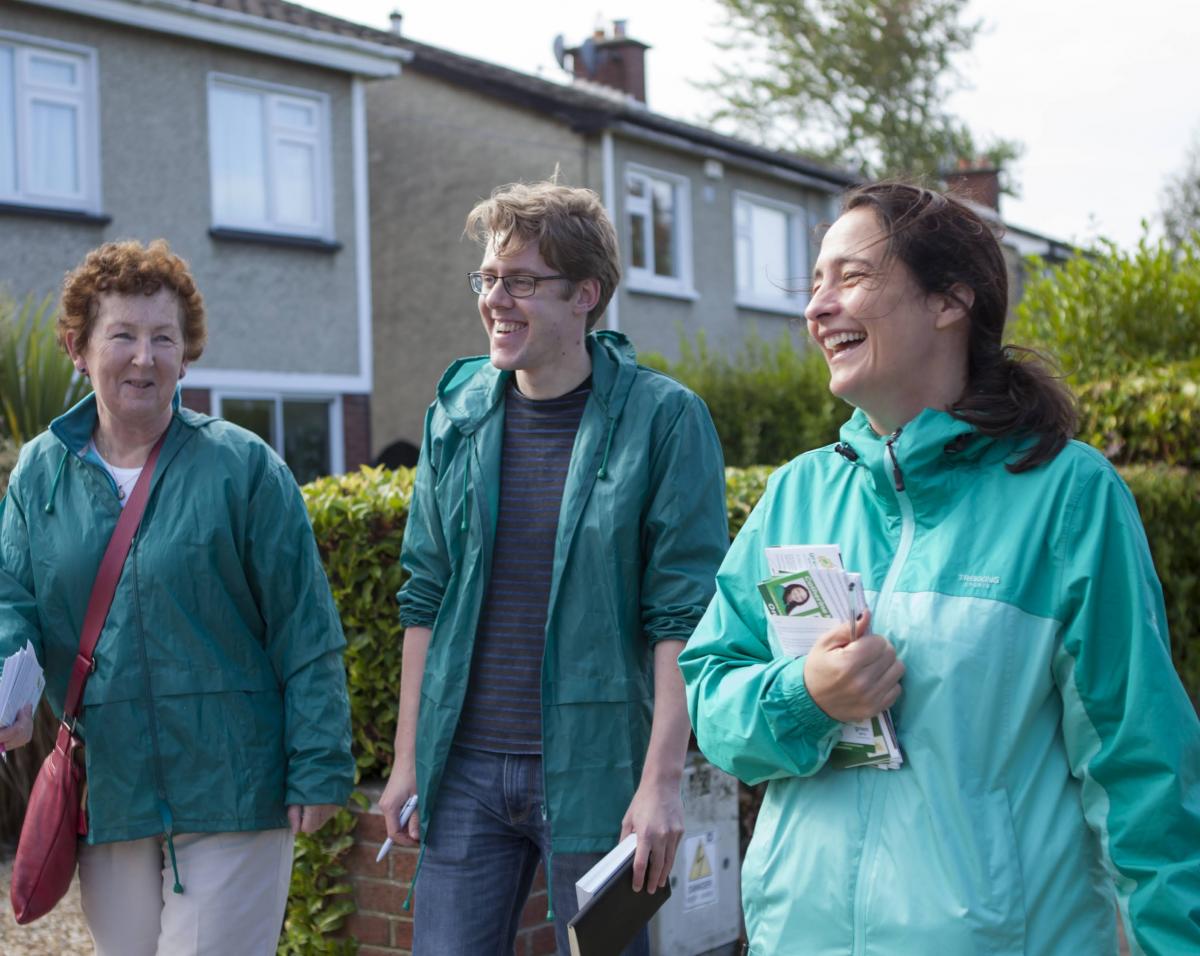 Three people in green jackets walking beside each other in a housing estate.