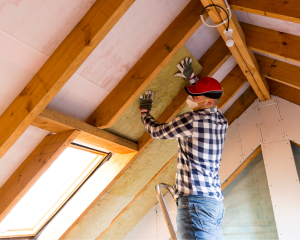 A man installing insulation in a home attic.