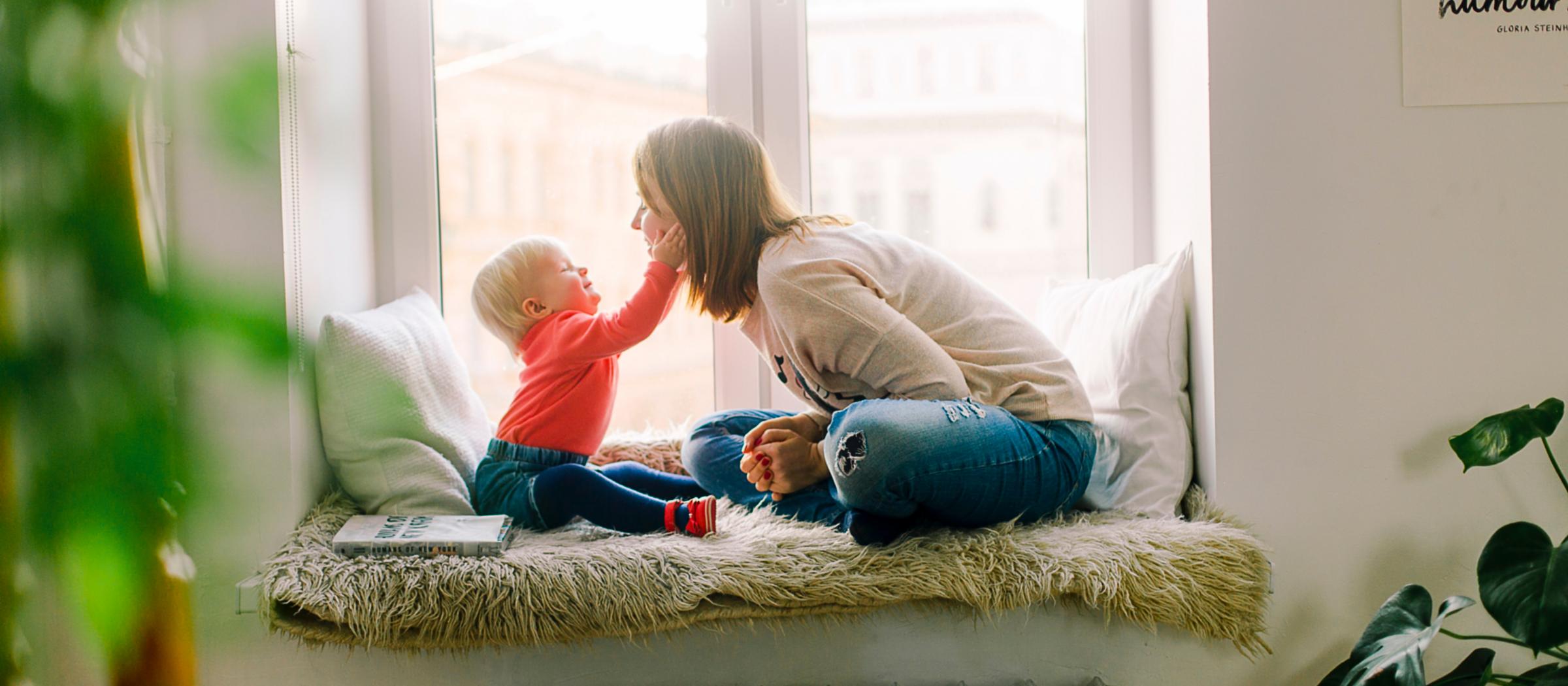 A mother and baby play on a window seat at home