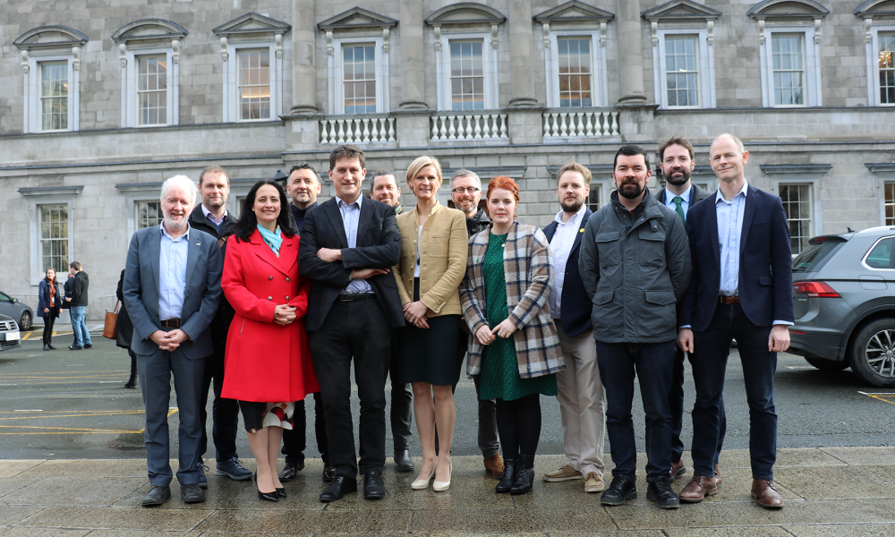 A photo of a group of people in suits and jackets standing in front of a large stone building, Leinster House.