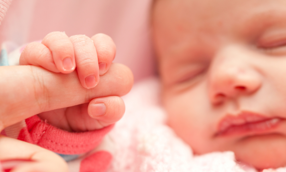 Newborn baby holds a parent's finger